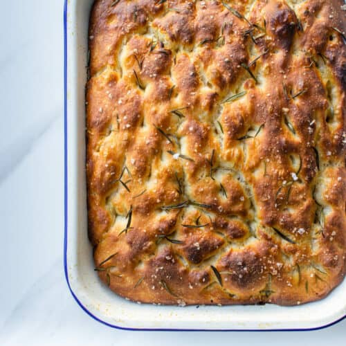Easy no knead focaccia topped with rosemary and salt on an oven tray