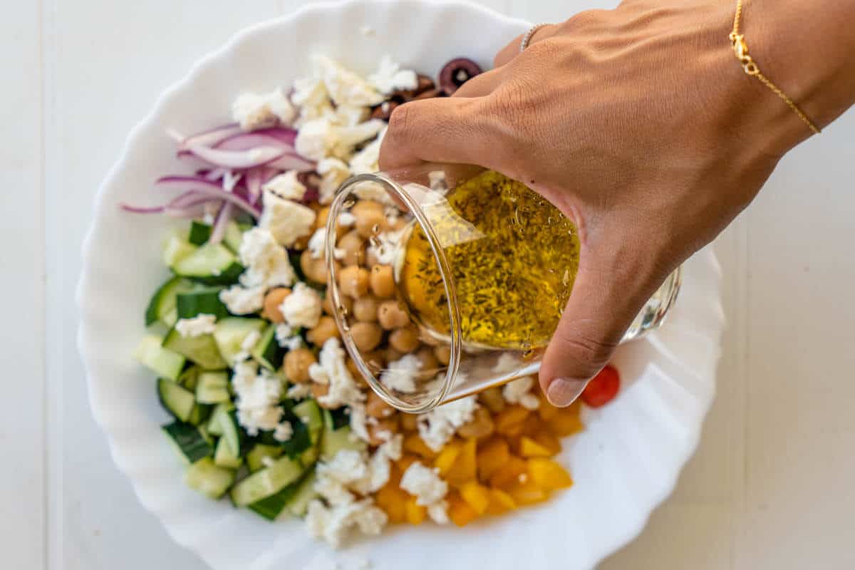 Salad dressing being poured on top of greek salad bowl
